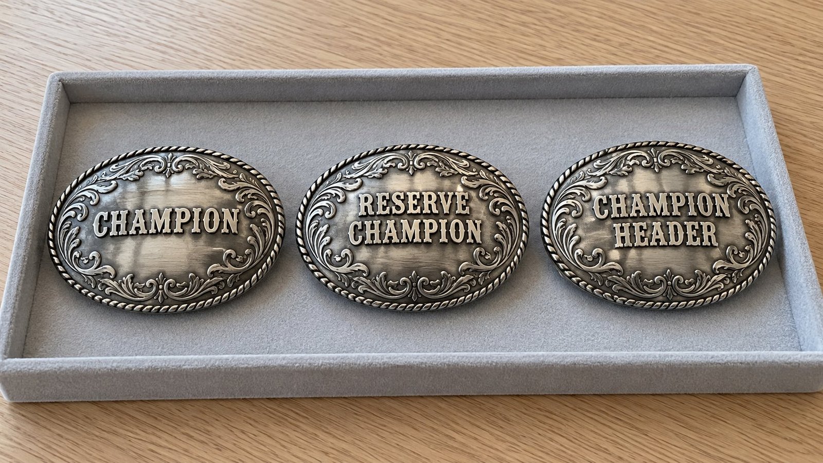 Matching rodeo award buckles labeled Champion, Reserve Champion and Champion Header